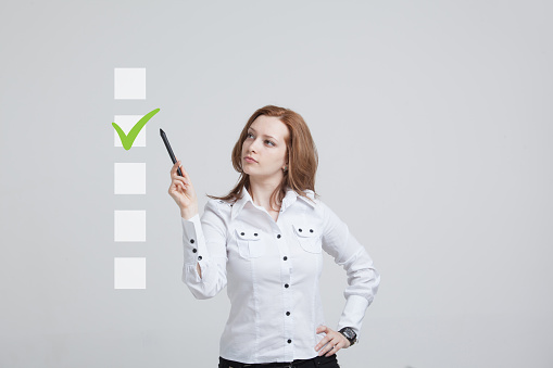 Young business woman checking on checklist box. Gray background. Concept on the topic of elections