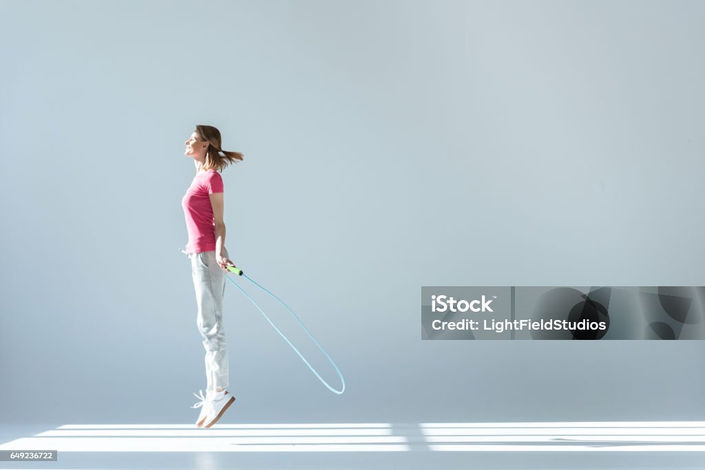 sporty woman exercising with skipping rope on grey side view of sporty woman exercising with skipping rope on grey Jumping Rope Stock Photo