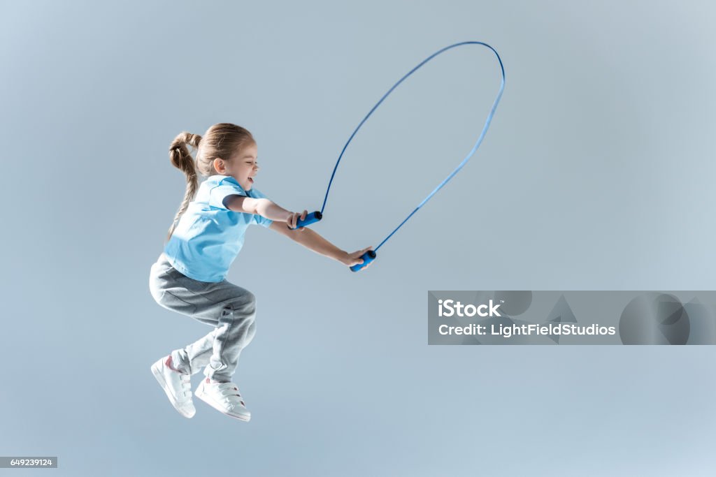 happy girl humping exercising with skipping rope on grey side view of happy girl humping exercising with skipping rope on grey Jumping Rope Stock Photo