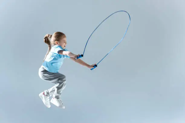 side view of happy girl humping exercising with skipping rope on grey