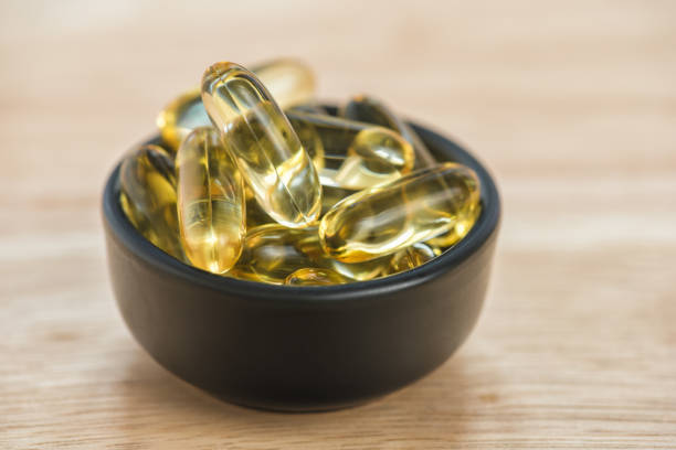 capsules de gel omega 3 d’huile de foie de morue dans le bol sur le bois de plancher - cod liver oil fish oil vitamin e vitamin pill photos et images de collection