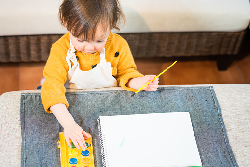 Three year old toddler painting a picture at home