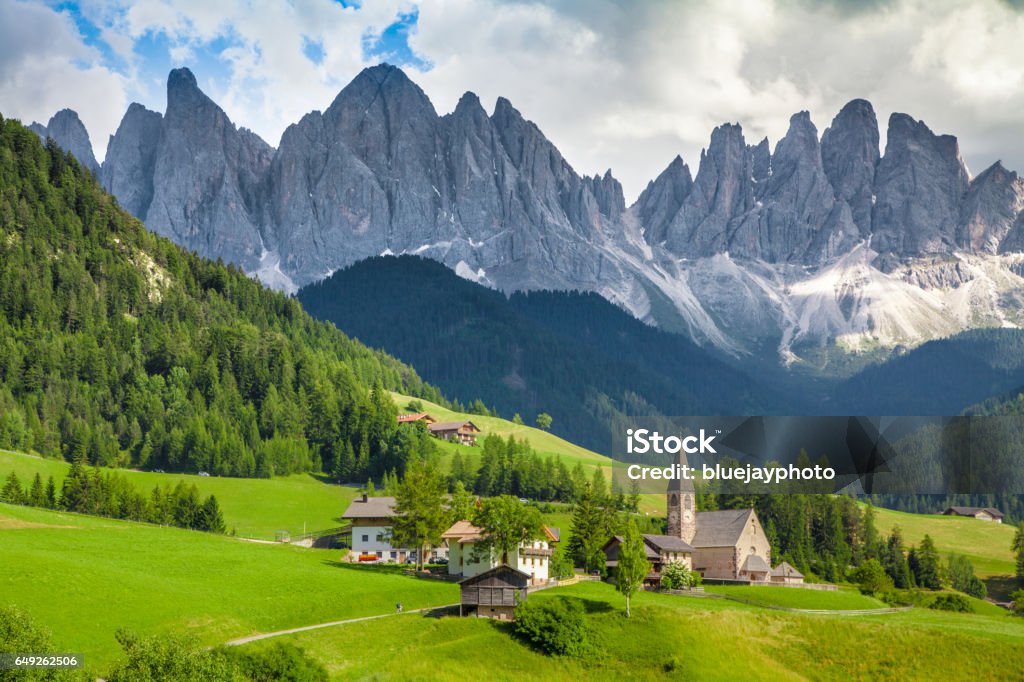 Val di Funes, South Tyrol, Italy Beautiful view of idyllic mountain scenery in the Dolomites with famous Santa Maddelana mountain village on a sunny day with blue sky and clouds in spring, Val di Funes, South Tyrol, northern Italy Alto Adige - Italy Stock Photo
