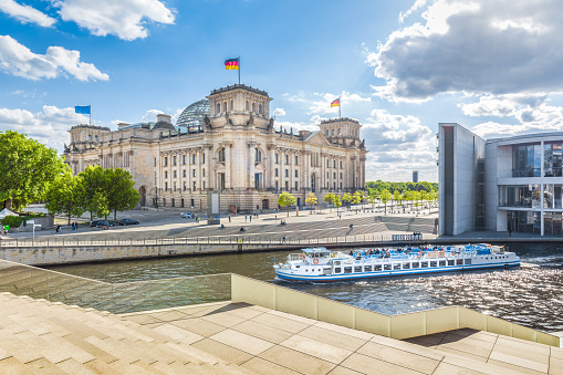 Panoramic view of Berlin government district with excursion boat on Spree river passing famous Reichstag building and Paul Lobe Haus on a sunny day with blue sky and clouds, Berlin Mitte, Germany