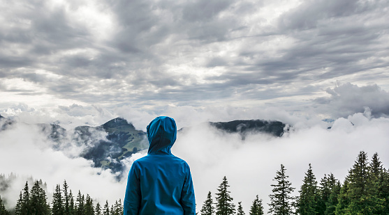 Young boy standing on the peak and looking to the misty landscape, in the Kitzbuhel mountains, Tirol, Austria