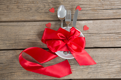 Cutlery and white plate tied up with red ribbon on wooden background