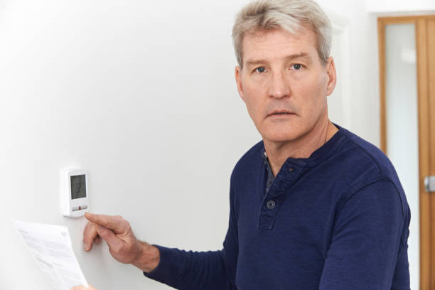 istock Worried Mature Man With Bill Turning Down Central Heating Thermostat 649285282