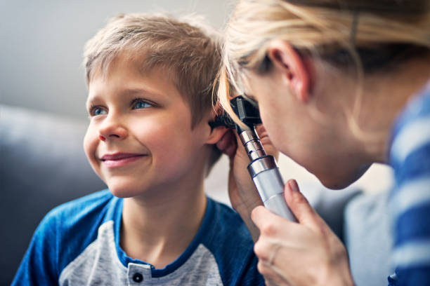 Happy little boy having ear exam Little boy having a medical ear examination. The smiling boy is aged 7. The doctor is vising boy at home and using otoscope to examine the boy's ear.
 ear photos stock pictures, royalty-free photos & images