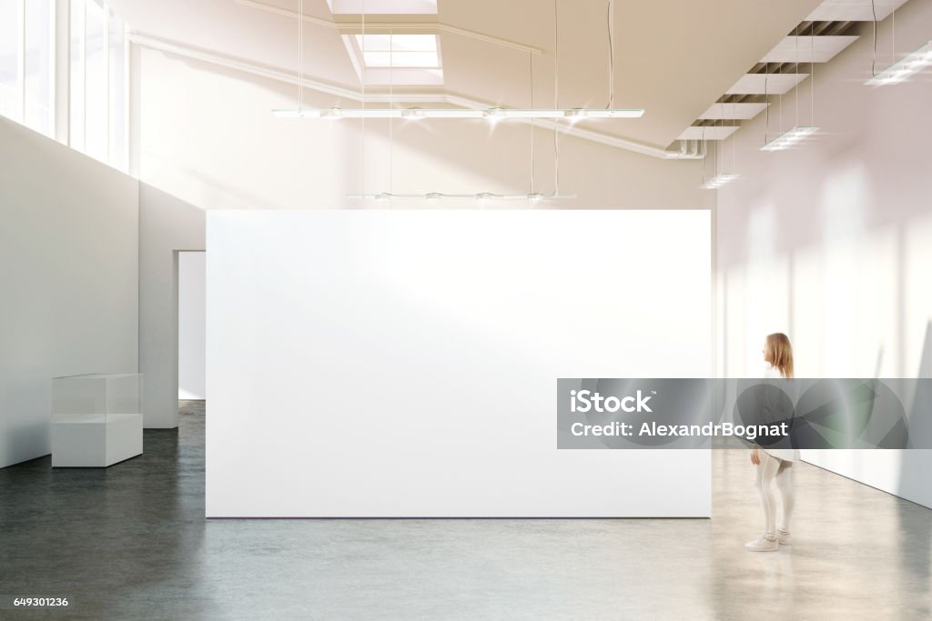 Woman walking near blank white wall mockup in modern gallery Woman walking near blank white wall mockup in modern gallery. Girl admires a clear big stand mock up in museum with contemporary art exhibitions. Large hall interior, banner exposition show Wall - Building Feature Stock Photo