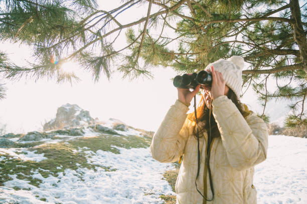 istock The girl in a White cap with a backpack in the winter in a forest looking through binoculars 649314916