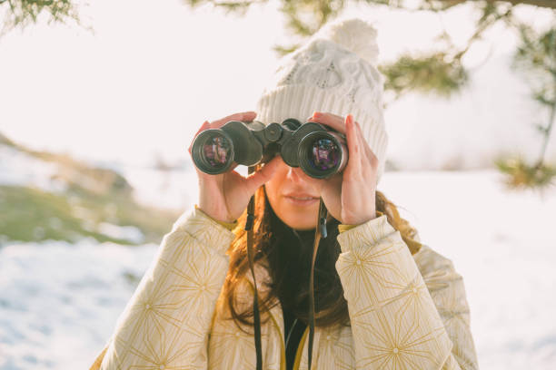 istock The girl in a White cap with a backpack in the winter in a forest looking through binoculars 649315078