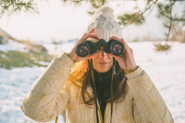 istock The girl in a White cap with a backpack in the winter in a forest looking through binoculars 649315180