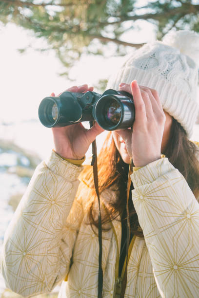 istock The girl in a White cap with a backpack in the winter in a forest looking through binoculars 649317458