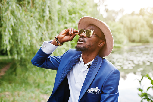 Portrait of stylish rich black man at blue jacket, hat and sunglasses