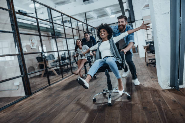 We are the winners! Four young cheerful business people in smart casual wear having fun while racing on office chairs and smiling race office stock pictures, royalty-free photos & images