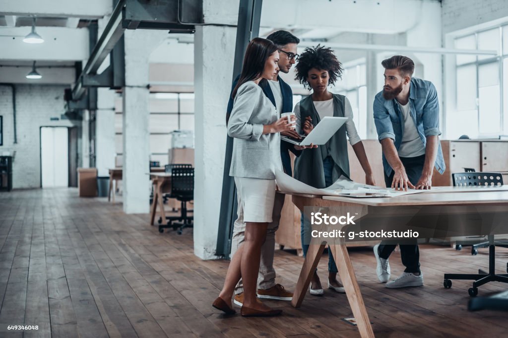 Working through some concepts. Group of young business people working together in creative office while standing near the wooden desk Office Stock Photo