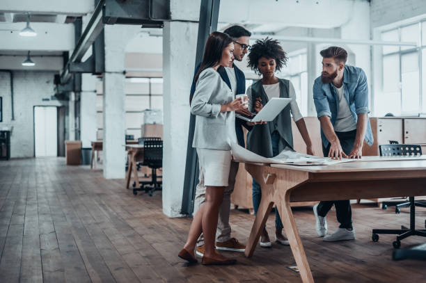 Working through some concepts. Group of young business people working together in creative office while standing near the wooden desk studio workplace stock pictures, royalty-free photos & images