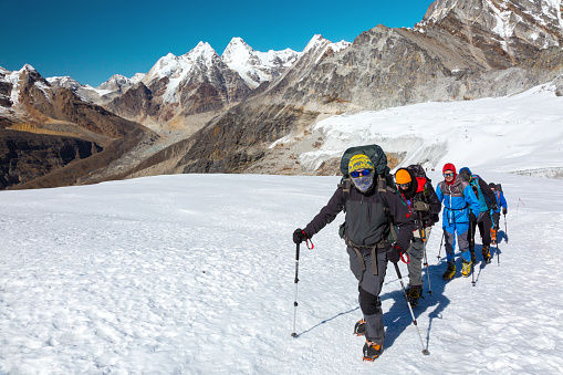 Severe Mountain Climbers in warm weather protective Clothing walking up on Glacier with climbing Gear and Backpacks against iconic Himalaya scenery on Background