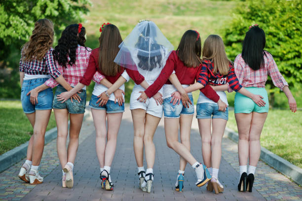 widok z tyłu siedmiu szczęśliwych i seksownych dziewczyn na krótkich spodenkach trzymających się za ręce na pośladkach i pozowanych na drodze w parku na wieczór panieński - bachelorette party zdjęcia i obrazy z banku zdjęć