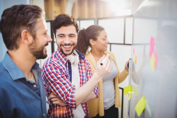 istock Happy executive with colleagues standing by whiteboard at creative office 649401806
