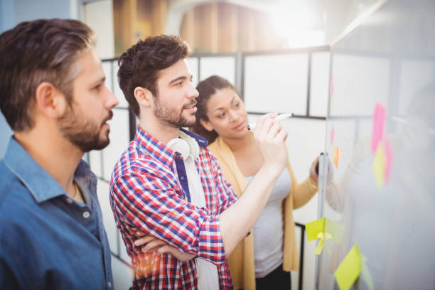 businessman with partners looking at whiteboard in creative office - writing whiteboard men businessman imagens e fotografias de stock