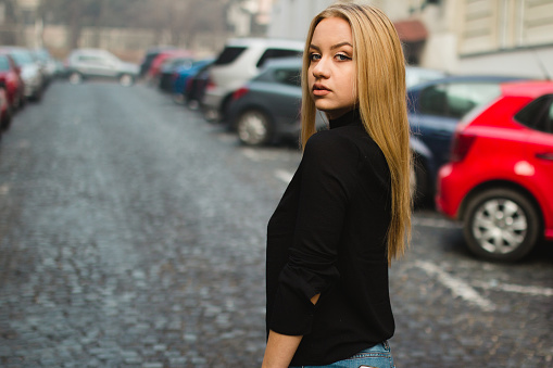 The beautiful blonde girl posing outside in autumn with casual clothes and standing. Young woman looking back through the camera.