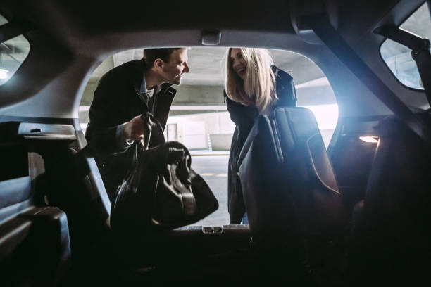 Couple at Airport Parking Garage A young couple embarking on a trip at the airport, carry-on luggage ready to go and prepared to travel the world.  They pull their belongings out of their car, leaving the vehicle in the terminal parking garage. disembarking stock pictures, royalty-free photos & images