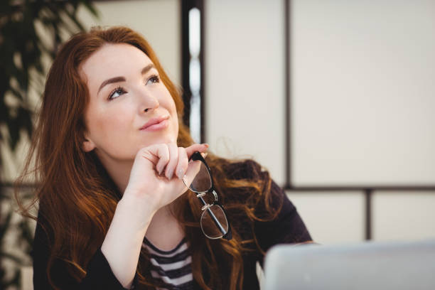 istock Thoughtful beautiful woman holding eyeglasses while looking up at creative office 649493242