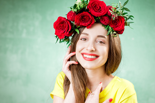 Colorful portrait of a beautiful woman in yellow t-shirt with wreath made of red roses on the green background