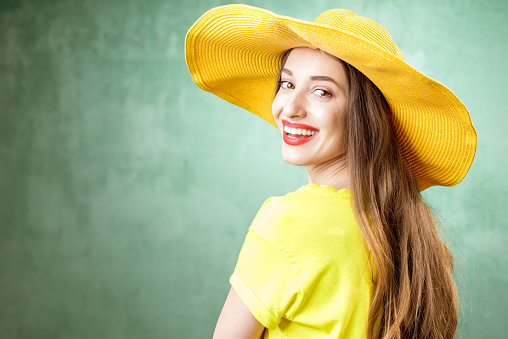Colorful portrait of a beautiful woman in yellow t-shirt and hat on the green background