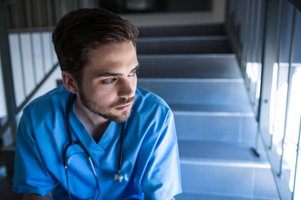 thoughtful male nurse sitting on staircase - single step imagens e fotografias de stock