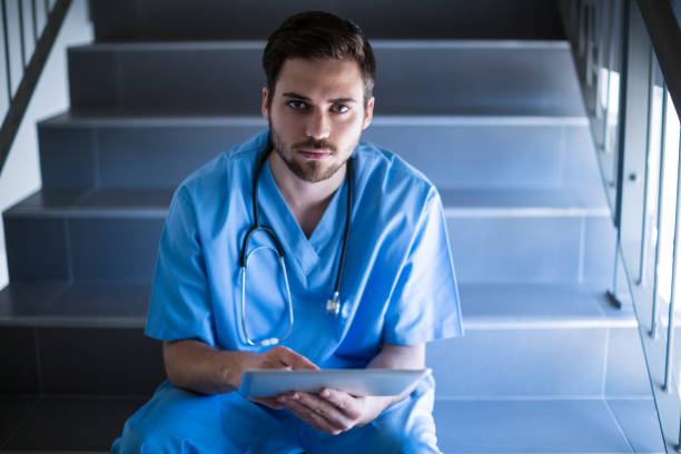 portrait of male nurse sitting on staircase and using digital tablet - single step imagens e fotografias de stock