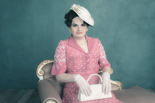 Trans woman retro 1920s fashion sitting on sofa with handbag.