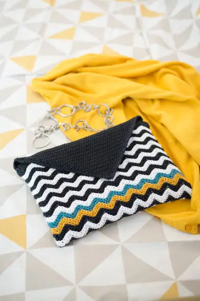 Crocheted envelope-style pouch with black and white with teal and gold wave pattern