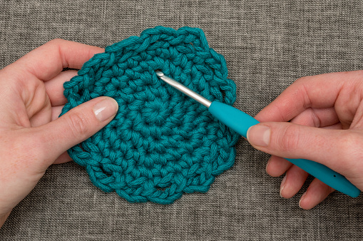 Knitting hook piercing a round teal crocheted coaster
