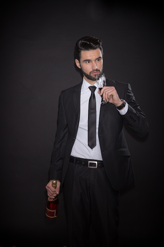 one young man elegant handsome, black background, suit jacket tie shirt pants, drinking bottle alcohol wine glass