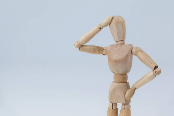 Confused wooden figurine standing with hand on head against white background