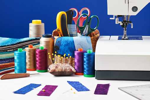 Sewing accessories in a basket and spools of threads next to sewing machine