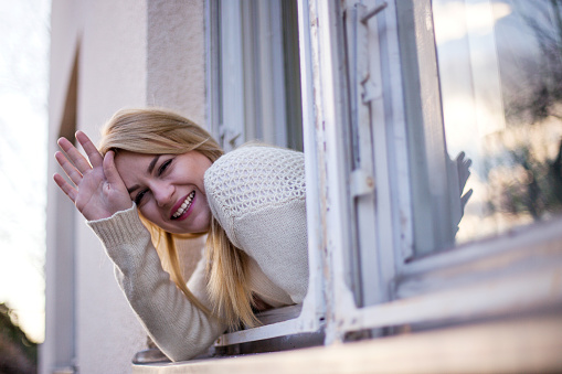 Blonde girl waving from window on sunny day