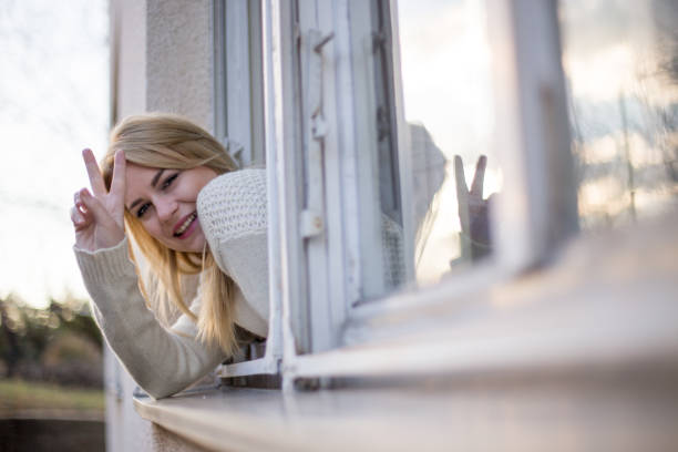istock Girl showing peace sign from house window 649594628