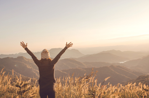Carefree Happy Woman Enjoying Nature on grass meadow on top of mountain cliff with sunrise. Beauty Girl Outdoor. Freedom