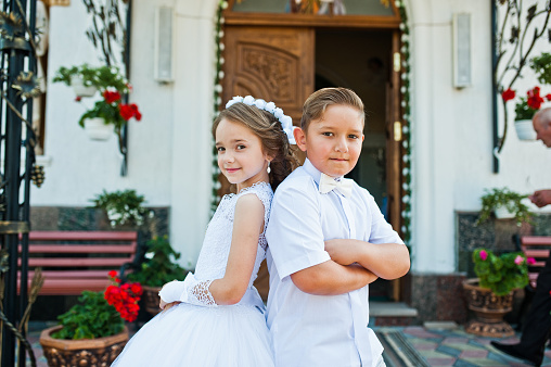 First holy communion, brother and sister stay at white dress background church