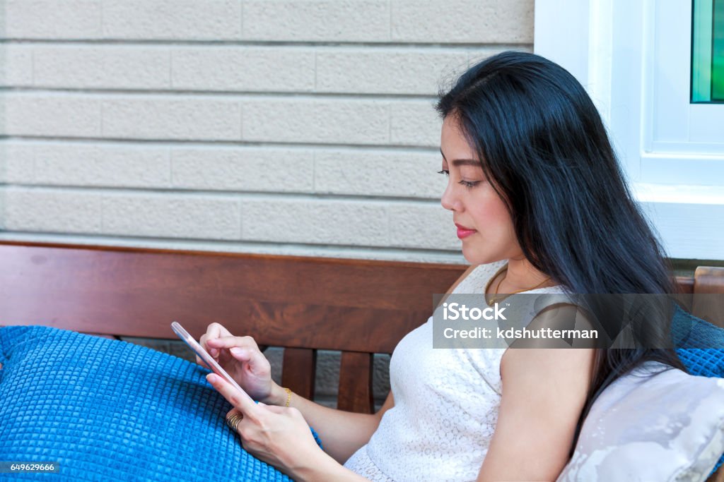 Asian woman typing text messages on smart phone. Side view of asian woman typing or reading text messages on smart phone at home. Businesswoman working with mobile phone. Adult Stock Photo