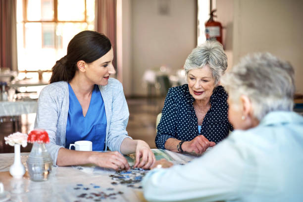 Shot of a young nurse helping two senior residents build a puzzle in a retirement home