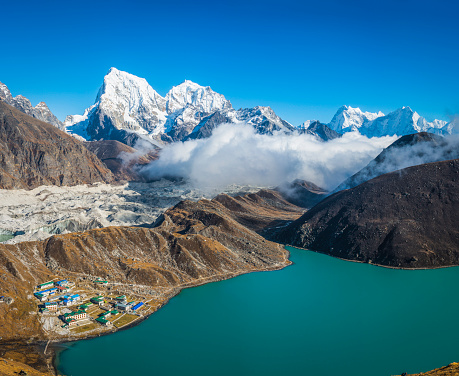 The snow capped summits of Tawoche (6542m) and Cholatse (6440m) overlooking the Sherpa village of Gokyo with its traditional teahouse lodges and blue glacial lake high in the Himalayan mountains of the Everest National Park, Nepal.