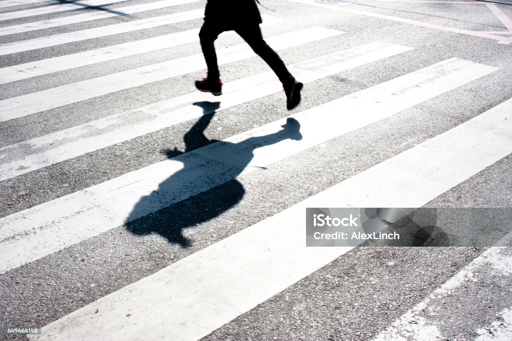 Kid's shadow on zebra crossing Blurry child's legs and kid's shadow with a backpack, on zebra crossing while running over the street in black and white Child Stock Photo