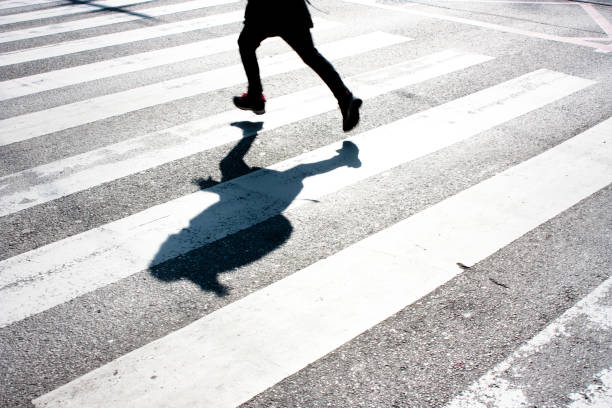 Kid's shadow on zebra crossing Blurry child's legs and kid's shadow with a backpack, on zebra crossing while running over the street in black and white crossing photos stock pictures, royalty-free photos & images