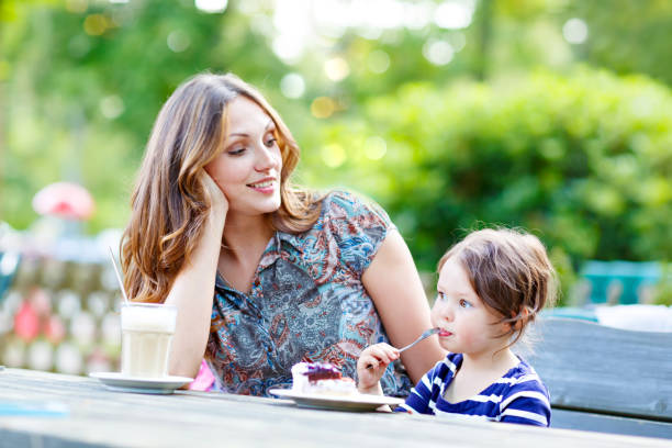 Mother and little adorable kid girl drinking coffee in cafe