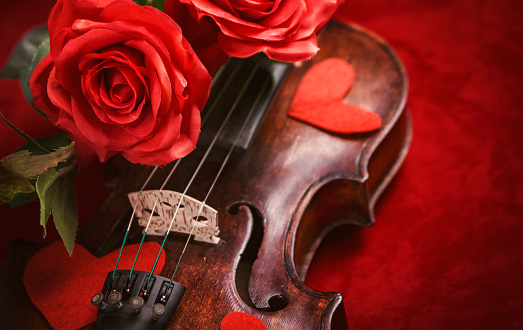 Antique wooden violin covered with roses and heart shapes on a red background, valentine's day or other romantic occasion