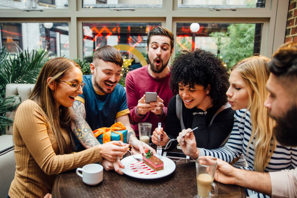 Struggling To Share Group of friends are sharing a slice of cake at a birthday party. One person is using his smart phone to take a photo. greed photos stock pictures, royalty-free photos & images